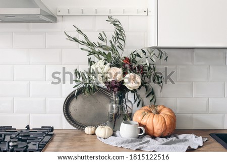 Autumn still life composition in rustic eclectic kitchen interior. Cup of coffee, vintage silver tray and floral bouquet. Wooden table background with pumkins. Thanksgiving, Halloween concept. 