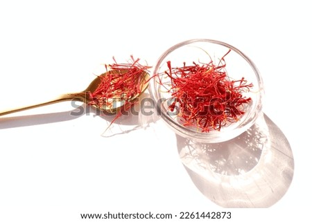 Autumn still life scene. Crocus sativus, commonly known as saffron crocus, is in a  glass bowl on a white background in sunlight. The crimson stigmas in a spoon.Long, harsh shadows. Minimal design.   