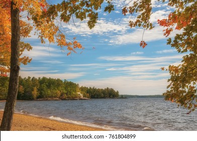 Autumn sunny day on the lake. autumn trees creating a frame, a small house cozy hidden among the trees on the shore. USA. Maine.
