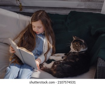 Autumn sunny weekend with cat at home. little girl reading a book on the veranda with pet, home education for children. stay at home, Children and Pets Relationships Concept