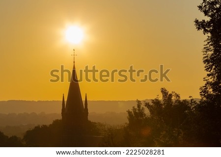 An autumn sunrise in Maastricht with in silhouette the tower of a church with the sun aligned above the religious Christian cross