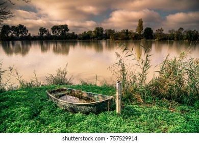 Autumn Sunset On A Waterway Of The Dordogne River Near Bordeaux In France With A Boat On The Grass.