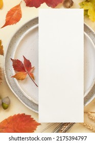 Autumn Table Place With Colorful Leaves And Blank Menu Card Top View. Mockup Of Fall Vertical Card On Light Yellowtable, Flat Lay, Copy Space. Harvest, Halloween And Thanksgiving Season