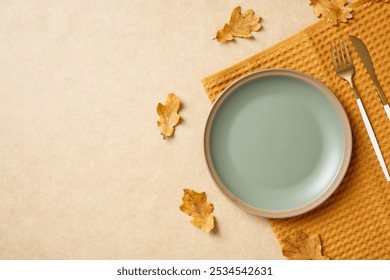 Autumn table setting with pastel green plate and golden cutlery on beige background, accented with fallen leaves. Thanksgiving dinner table serving, top view. - Powered by Shutterstock