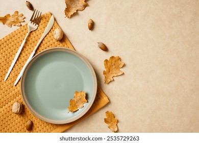 Autumn table setting with a pastel green plate, gold cutlery, and scattered leaves on a textured beige background - Powered by Shutterstock