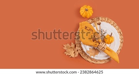 Autumn table setting with pumpkin decorations on orange background. Empty plate, yellow napkin and dry leaves. Autumn holiday mood, Halloween, Thanksgiving top view banner with copy space
