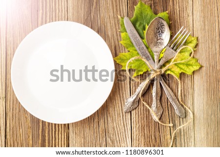 Autumn Table setting. Thanksgiving dinner plate with fork, knife and leaves on rustic wooden table background. Top view, copy space, place for text, toned