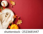 Autumn table setting with white plate, gold cutlery, beige napkin, and decorations of pumpkins, acorns, and fall branches on a deep red background. Thanksgiving dinner concept.