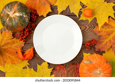 Autumn Table For Thanksgiving Dinner. Top View Of Maple Leaf On A White Empty Plate And Fallen Colored Leaves On A Wooden Table. The Concept Of Autumn Food.