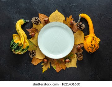 Autumn And Thanksgiving Day Table Setting With Fallen Leaves, Decorative Pumpkins, The Empty White Plate On The Dark Background