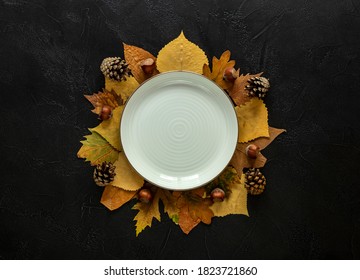 Autumn And Thanksgiving Day Table Setting With Fallen Leaves And The Empty White Plate On The Dark Background