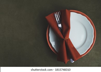 Autumn Thanksgiving setting table. Plates, fork, knife with serving napkin on dark green tablecloth. Vintage style. Top view, flat lay, copy space