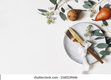 Autumn Thanksgiving Table Place Setting. Golden Cutlery, Porcelain Plate, Berry Eucalyptus Leaves And Branches, Silk Ribbon And Pear Fruit On White Table Background. Fall Wedding. Flat Lay, Top View.