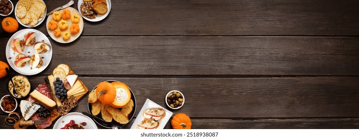 Autumn theme appetizer corner border against a dark wood banner background. Charcuterie board, pumpkin and apple dips, crostini, cheeses and snacks. Overhead view.