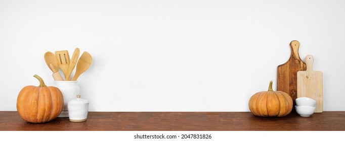 Autumn Theme Kitchenware, Utensils And Pumpkins On A Wooden Shelf Or Counter. Banner Against A White Wall Background With Copy Space. Fall Home Kitchen Cooking Concept.