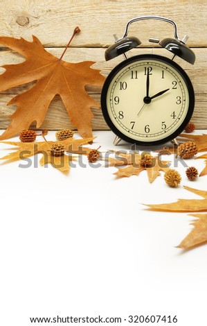 Autumn Time Change / Fall Back / Maple Leaves and an Alarm Clock on a Wooden Background