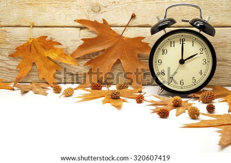 Autumn Time Change / Fall Back / Maple Leaves and an Alarm Clock on a Wooden Background