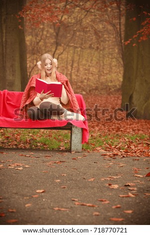 Autumn time education concept. Blonde girl with book. Attractive woman sitting on blanket in the park relaxing, foggy misty day