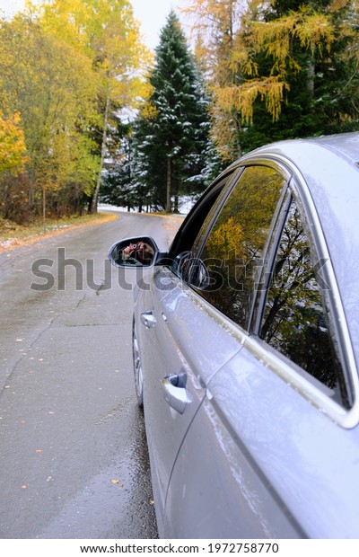 Autumn travel and trips.\
Road view.First snow. Travel by car. Car on the autumn road.Silver\
color car on the road with autumn bright trees and the  snow. Late\
fall season.