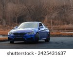 Autumn vibes hit an blue sport car in a empty parking lot with the forest in background.