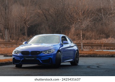 Autumn vibes hit an blue sport car in a empty parking lot with the forest in background.