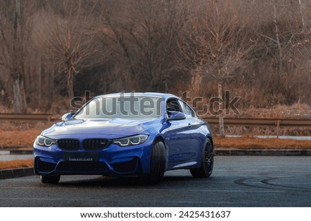 Autumn vibes hit an blue sport car in a empty parking lot with the forest in background.