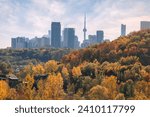 Autumn view from the hill in Weston Family Quarry Garden with hazy silhouettes of skyscrapers and CN Tower in Downtown Toronto in background and yellow orange red trees in foreground