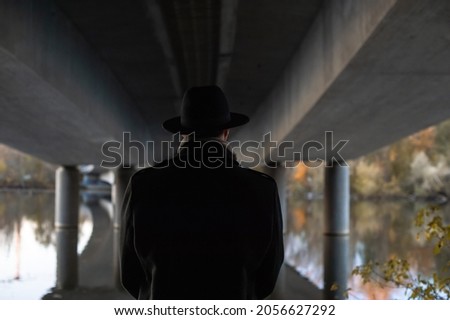Autumn walk. Portrait of a man in a black coat and hat under the bridge