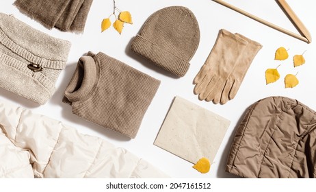 Autumn warm clothing beige colored, folded knitted wear, hat, scarf, gloves, sweater with craft paper for copy space. Flat lay from female fashion autumnal outerwear for cold weather in fall season.