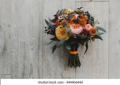 Autumn Wedding Bouquet Made Of Orange Flowers Lies On The White Wooden Table