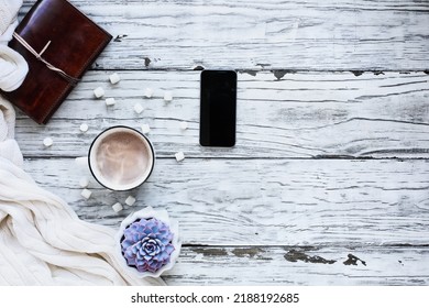 Autumn Or Winter Background Shot From Top View With Hot Cocoa, Houseplant, Cell Phone, Book, And Throw Blanket Over Rustic White Wood Table. Overhead Top View.