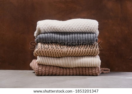 Autumn or winter comfort concept,Stack of warm cozy knitted womens sweaters on gray background.

