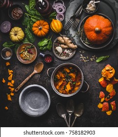 Autumn And Winter Cooking And Eating With Pumpkin Dishes. Vegetarian Stew In Cooking Pot With Spoon And Vegetables Ingredients On Dark Kitchen Table Background, Top View. Healthy Seasonal Food 