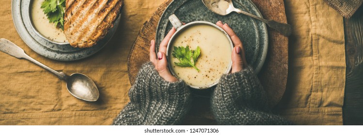 Autumn, Winter Home Dinner. Flat-lay Of Fall Warming Celery Cream Soup, Grilled Bread And Female Hands Over Linen Tablecloth, Top View, Wide Composition. Comfort Food, Healthy And Slow Food Concept