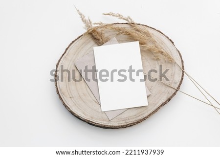 Autumn, winter stationery still life. Blank greeting card, invitation mockup on cut wooden round board. Craft envelope and dry festuca grass. Flatlay, top view. Minimal neutral boho fall template.