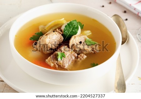 Autumn winter warming beef broth with a piece of meat and vegetables in a white dish on light background. Close up.