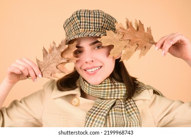 Autumn woman, fall leaves season. Autumn mood. Happy smiling woman holding in her hands yellow leaves covering her face over beige background.