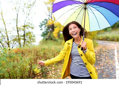 Autumn Woman Happy In Rain Running With Umbrella. Female Model Looking Up At Clearing Sky Joyful On Rainy Fall Day Wearing Yellow Raincoat Outside In Nature Forest By Lake. Multi-ethnic Asian Girl.