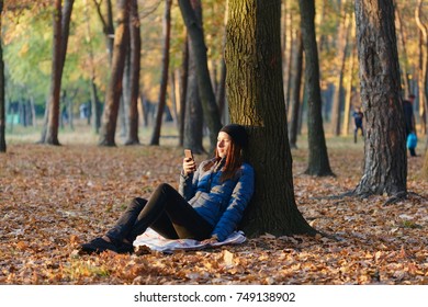 Autumn woman under a tree in autumn park communicates via the Internet using a smartphone - Shutterstock ID 749138902