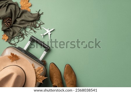 Autumnal allure ready for takeoff. Top view of petite plane, adorned with fall fashion essentials: hat, plaid poncho, ankle boots, suitcase, leaves, cone on muted green backdrop with space for text