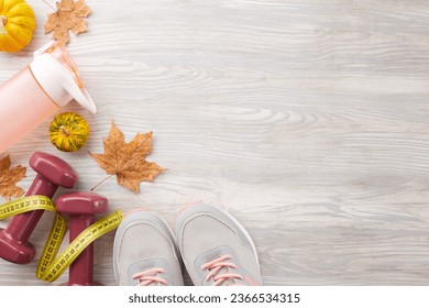 Autumnal muscle growth concept. Top view photo of trendy sneakers, tape measure, dumbbells, plastic bottle, pumpkins, fallen leaves on light wooden background with promo spot - Shutterstock ID 2366534315
