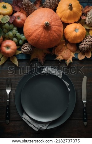 Autumnal table setting with pumpkins, drying leaves , black plates on dark background. Happy Holiday. Thanksgiving Day. Vertical. View from above.