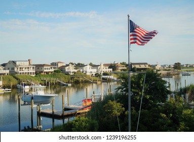 Avalon, New Jersey – July 18, 2014: An American Flag In Front Of A Row Of Luxury Waterfront Vacation Homes On The Back Bay In Avalon, New Jersey.