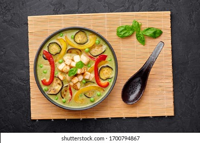 aVegetarian Thai Green Curry with tofu in black bowl at dark slate background. Veg Green Thai Curry is thailand cuisine dish with green chillies paste, basil, spices and vegetables. Thai Food