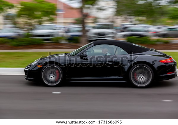 Aventura, Florida/USA - May 14, 2020: Black Porsche 911\
Turbo Cabriolet on a speed outdoor, long exposure effect on\
background.  