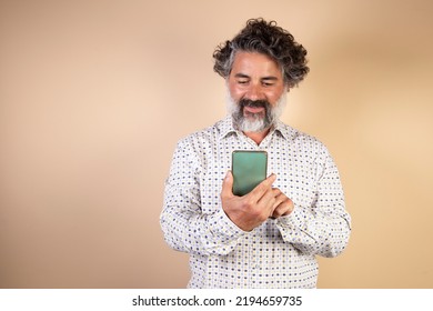 An Average Adult Sends Phone Messages On A Smart Phone. Smiling Modern Man Using Smartphone On Light Wall. Happy Man Using App On Mobile Phone.