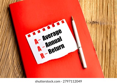 Average annual return concept on paper note with acronym aar on red notebook and pen over wooden desk. 