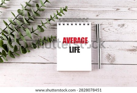 Average life concept with notebook, pen and green leaves on white wooden background, representing lifespan, longevity.