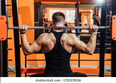 Average Plan, Back View. A Muscular Man Dressed In Black Sportswear Is Training Muscles, Biceps And Triceps - With An Effort He Raises The Bar. Fitness And Sport. Healthy Lifestyle Concept