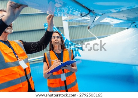 Aviation engineers collaborating on a thorough inspection of an airplane wing inside a hangar, ensuring safety and quality control for aeronautical maintenance operations
